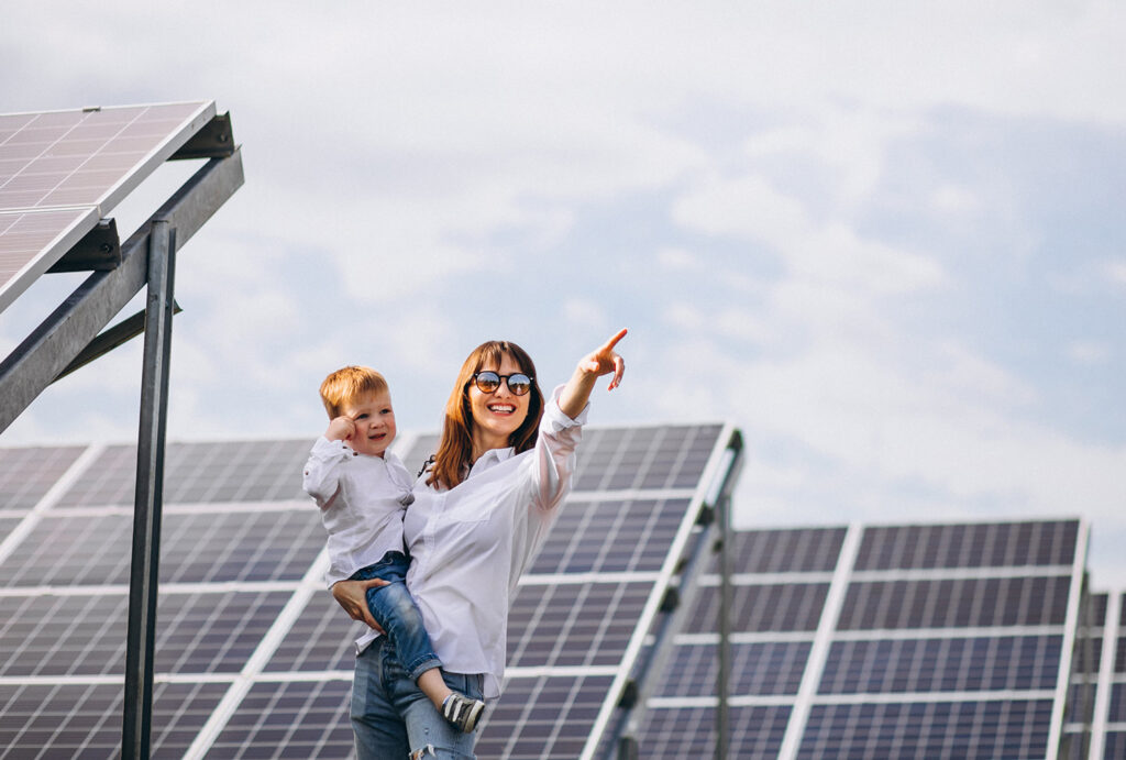 Madre e hijo señalando el cielo con expresión de felicidad. De fondo un campo de paneles solares.